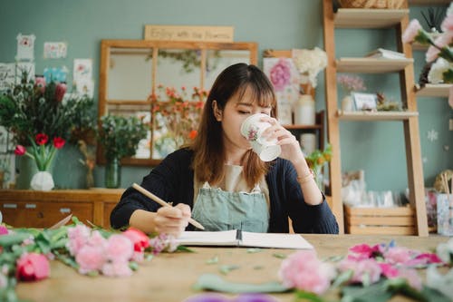 在花店工作时喝咖啡的亚裔女子 · 免费素材图片