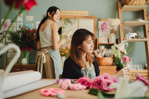 严重的亚洲花店，在和同事一起工作期间制作花束 · 免费素材图片