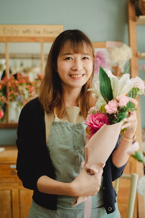 站立与花束的快乐的亚裔女性卖花人在商店 · 免费素材图片