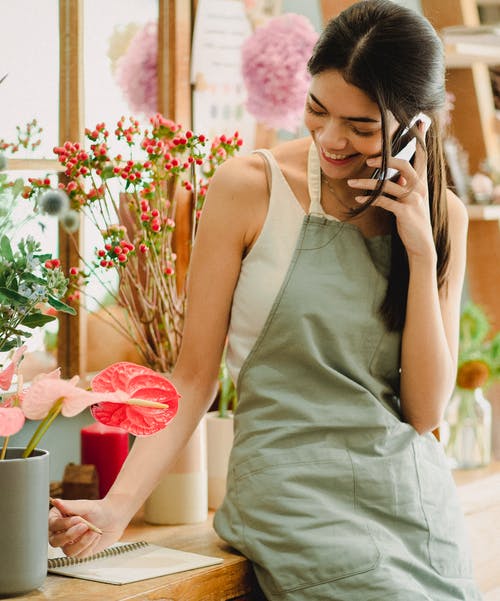 微笑的女性花店谈话在花店的电话 · 免费素材图片