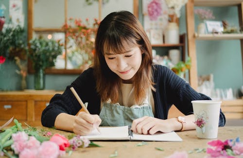 美满的亚洲女人写在花店里的抄写本 · 免费素材图片