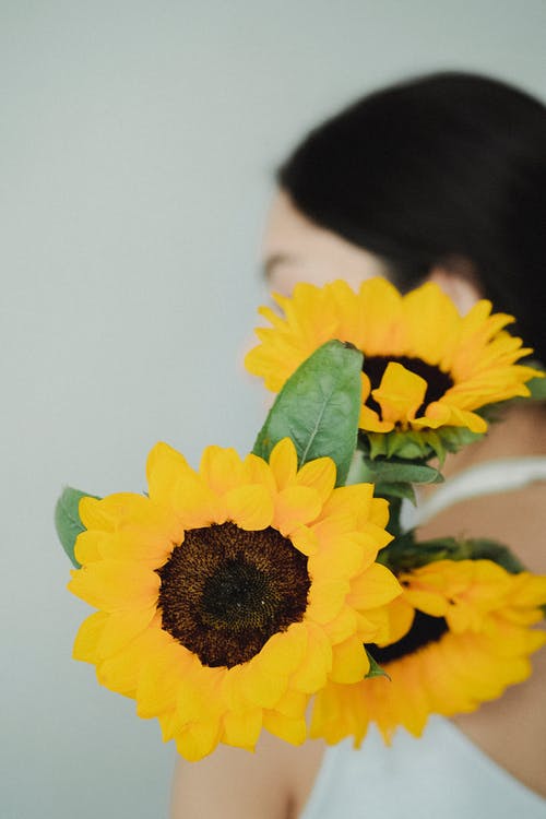 明亮的黄色向日葵在肩膀上的匿名女人 · 免费素材图片