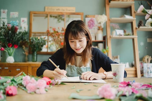 在创造性的花卉商店在笔记本的微笑的亚裔妇女文字 · 免费素材图片