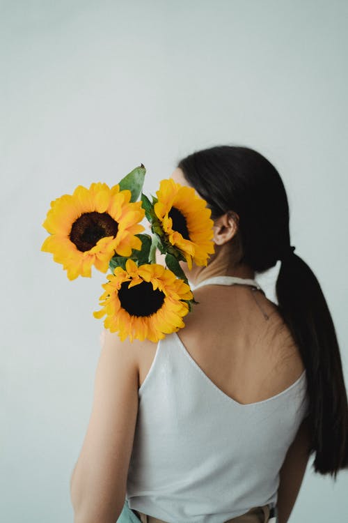平静的女性在肩膀上抱着向日葵 · 免费素材图片