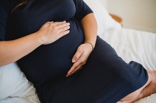 匿名的孕妇在床上爱抚腹部 · 免费素材图片