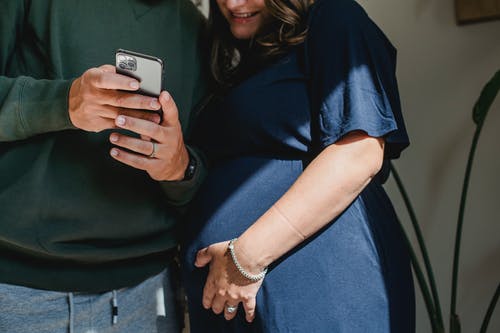 裁剪孕妇和丈夫在家共享智能手机 · 免费素材图片