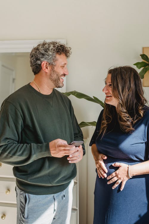 性格开朗的孕妇与丈夫与智能手机在家里说话 · 免费素材图片