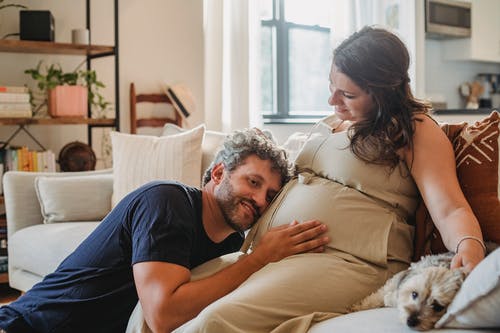 性格开朗怀孕夫妇与狗在沙发上 · 免费素材图片