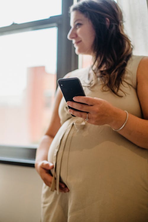 怀孕的女性，站在房间里时使用手机 · 免费素材图片