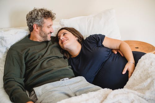 在舒适的床上拥抱怀孕的妻子的男人微笑着 · 免费素材图片