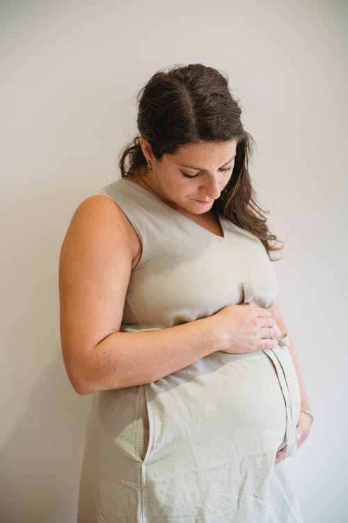 看下来在腹部的年轻孕妇反对白色背景 · 免费素材图片