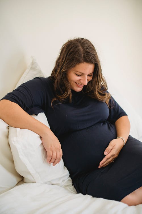 微笑的孕妇在柔软的床上抚摸肚子 · 免费素材图片