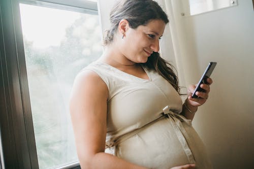 孕妇在房间里的电话上发短信 · 免费素材图片