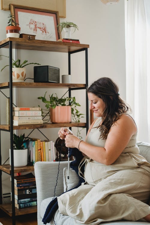 美满的孕妇在沙发上编织 · 免费素材图片