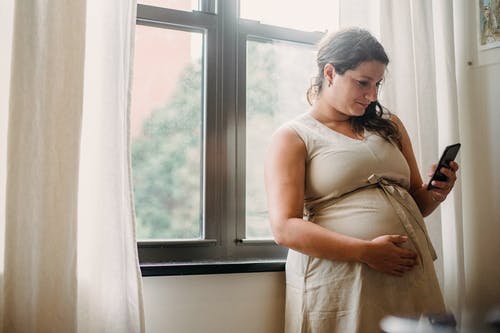 孕妇在家站立时使用手机 · 免费素材图片