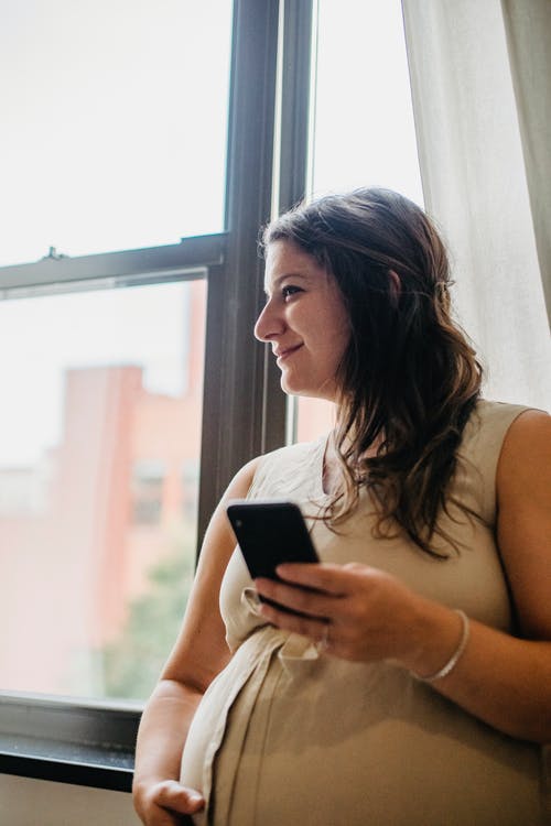 孕妇在家站立时使用电话 · 免费素材图片