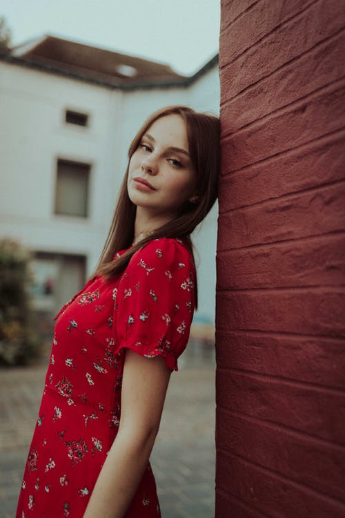 倚在红砖墙上的红色和白色的花衬衫的女孩 · 免费素材图片