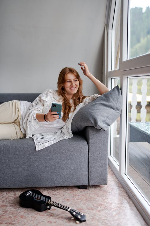 有智能手机的懒人微笑的妇女懒洋洋地在房子里的沙发上 · 免费素材图片