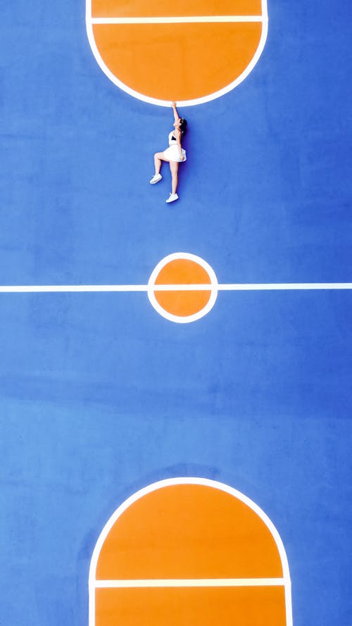 运动服和运动鞋躺在蓝色运动场上的女人 · 免费素材图片