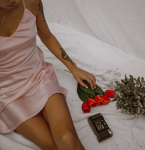 作物诱人的女人坐在床上用鲜花和复古相机拍照 · 免费素材图片