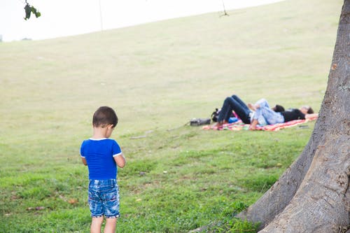 不可识别的男孩在草地上对休息的父母在夏天 · 免费素材图片