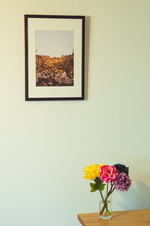 在花瓶里的七彩花朵木制的桌子上放在附近的相框照片墙 · 免费素材图片