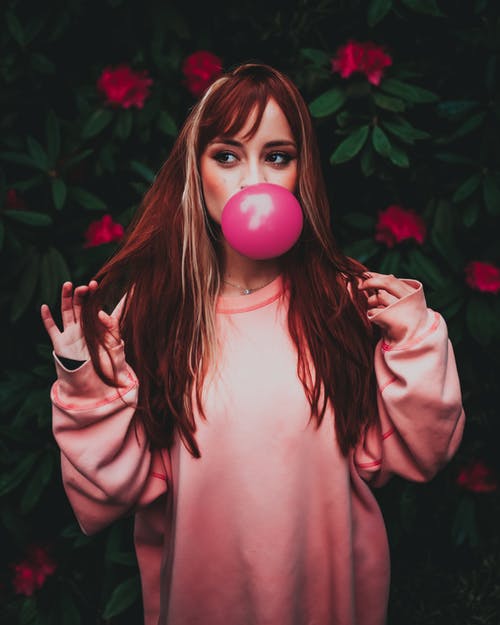 在花园里吹粉色口香糖的时髦衣服的梦幻女人 · 免费素材图片