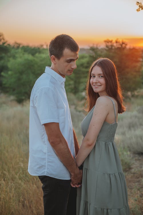 握手的愉快的年轻夫妇在草甸在日落 · 免费素材图片