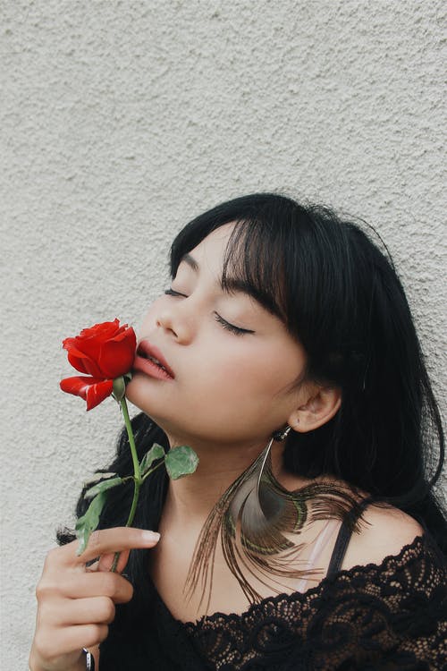 感性的亚洲女士，嗅到红玫瑰白墙上 · 免费素材图片