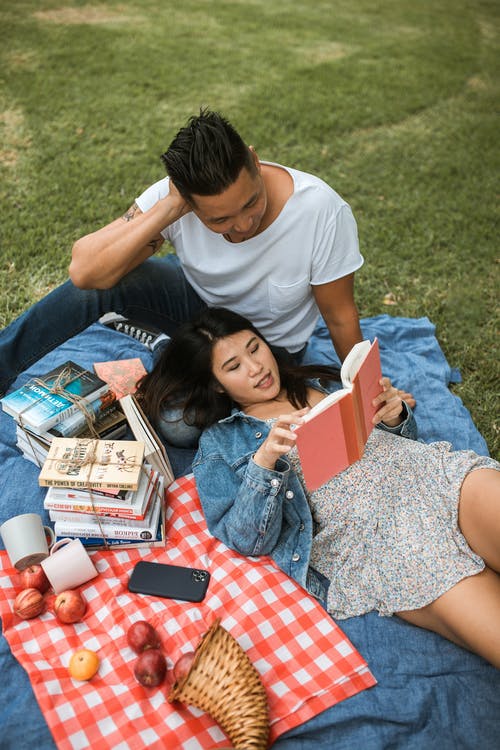 白色t恤的女孩坐在蓝色牛仔牛仔裤阅读的女孩旁边的蓝色纺织上 · 免费素材图片