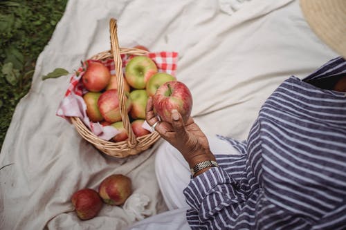 拿着苹果的种族妇女坐在毯子在庭院里 · 免费素材图片