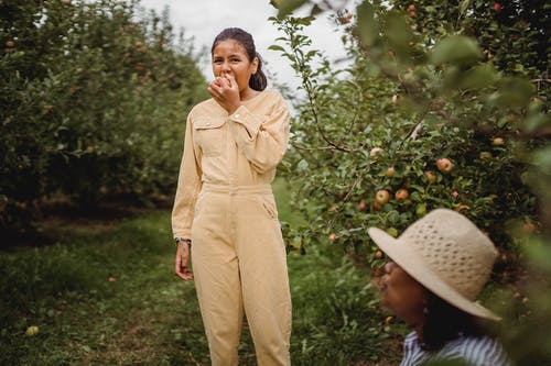 族裔女孩在花园里咬苹果 · 免费素材图片