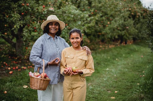 高兴的族裔母亲带着女儿和装满苹果的篮子 · 免费素材图片
