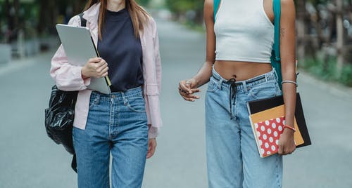 作物多种族的女学生背着笔记本电脑和笔记本沿着公园散步 · 免费素材图片