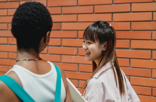 积极的多民族女学生一起走在砖砌建筑外面 · 免费素材图片