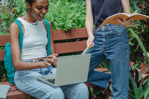 使用便携式计算机的快乐的黑人妇女与朋友的研究 · 免费素材图片