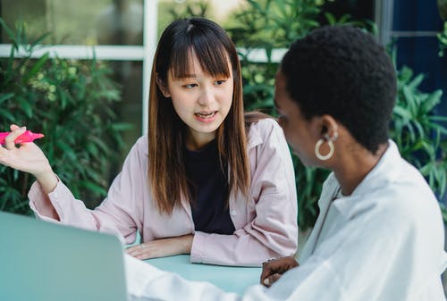 亚裔妇女讲话与黑人女朋友在桌上在庭院里 · 免费素材图片