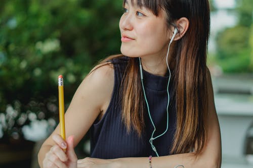 听到音乐的愉快的年轻亚裔学生，当学习在桌上在公园时 · 免费素材图片