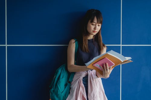 有练习本的集中的亚裔学生学习在蓝色墙壁附近的 · 免费素材图片
