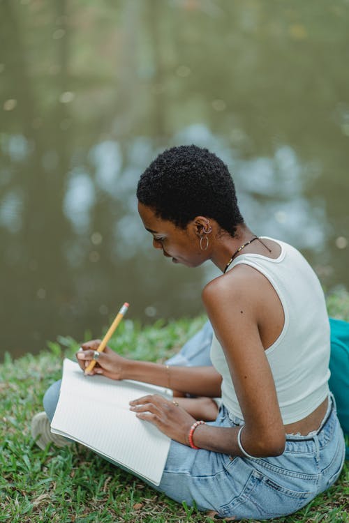 严重的黑人学生在公园里的笔记本中写论文 · 免费素材图片