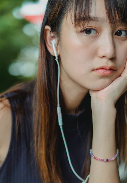 戴着耳机在手上倾斜的年轻女子 · 免费素材图片