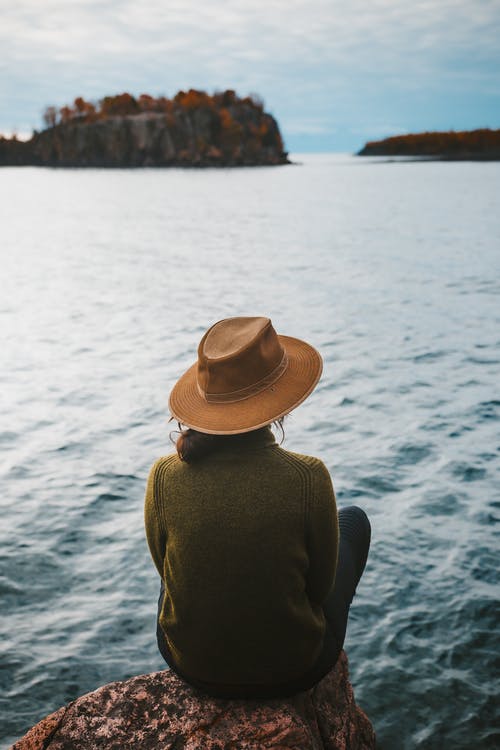 棕色的帽子和黑色的长袖衬衫，坐在海边的人 · 免费素材图片