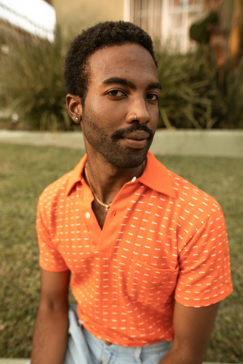 橙色按钮衬衫站在绿草地上的男人 · 免费素材图片