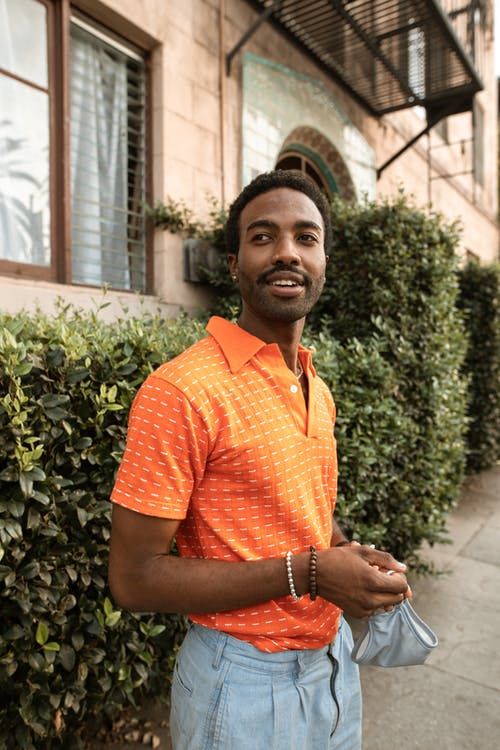 橙色马球衬衫站在绿色的植物附近的人 · 免费素材图片