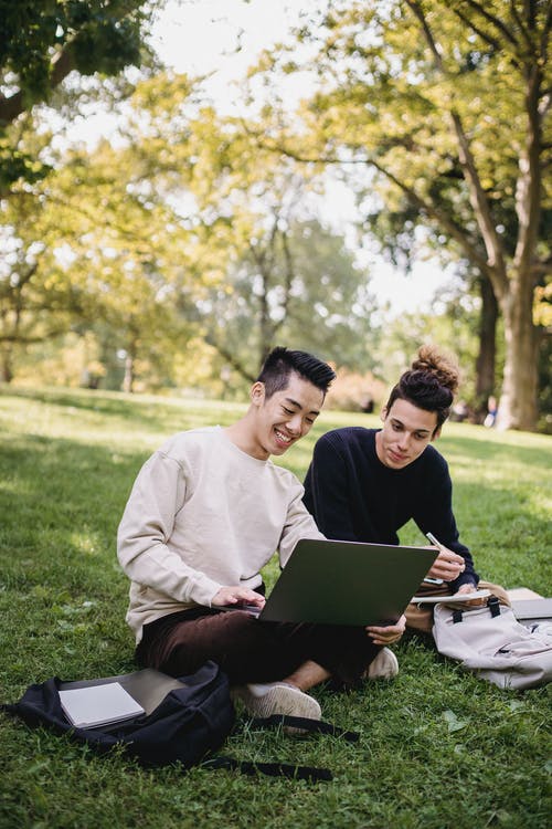 性格开朗的族裔男学生在公园草坪上的作业上工作 · 免费素材图片