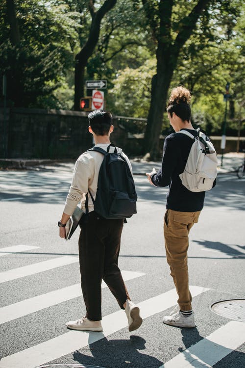 匿名的年轻人过马路在绿树附近在阳光下 · 免费素材图片