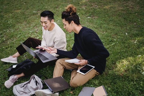 在公园的草坪上一起学习的满足的族裔男学生 · 免费素材图片