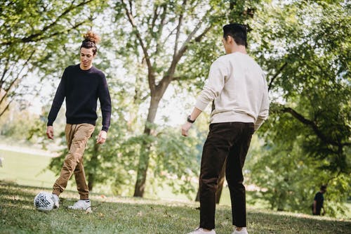 积极的族裔男性朋友在公园里踢足球 · 免费素材图片