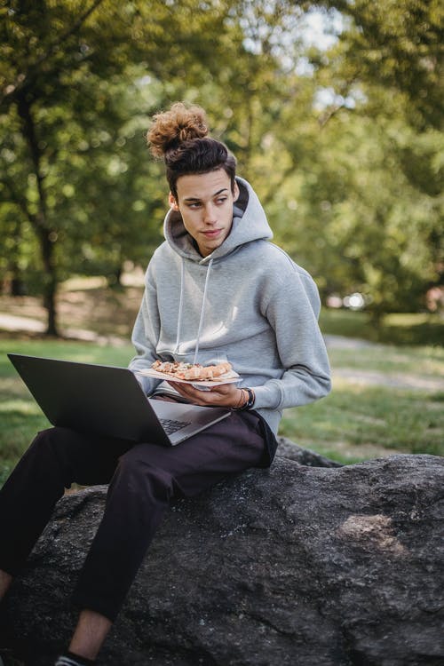 灰色连帽衫坐在岩石上使用笔记本电脑的人 · 免费素材图片