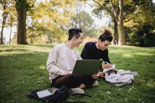 男人和女人坐在绿草地上使用便携式计算机 · 免费素材图片